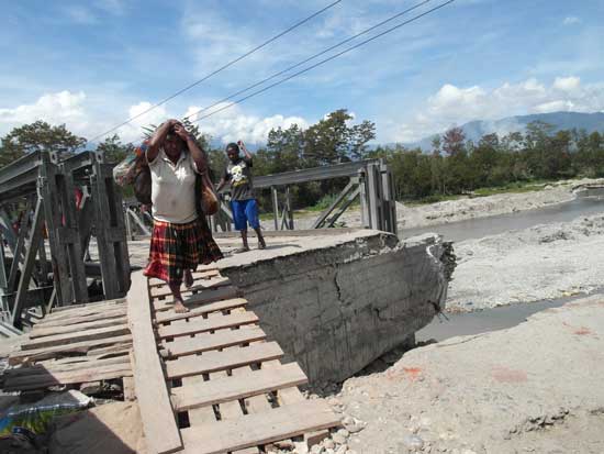 A woman carries vegetables to market across a half-collapsed bridge in Wamena, Papua, Indonesia
